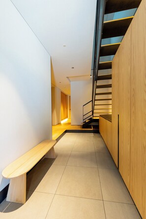A modern interior with a wooden bench, a staircase, and a hallway leading to another room.