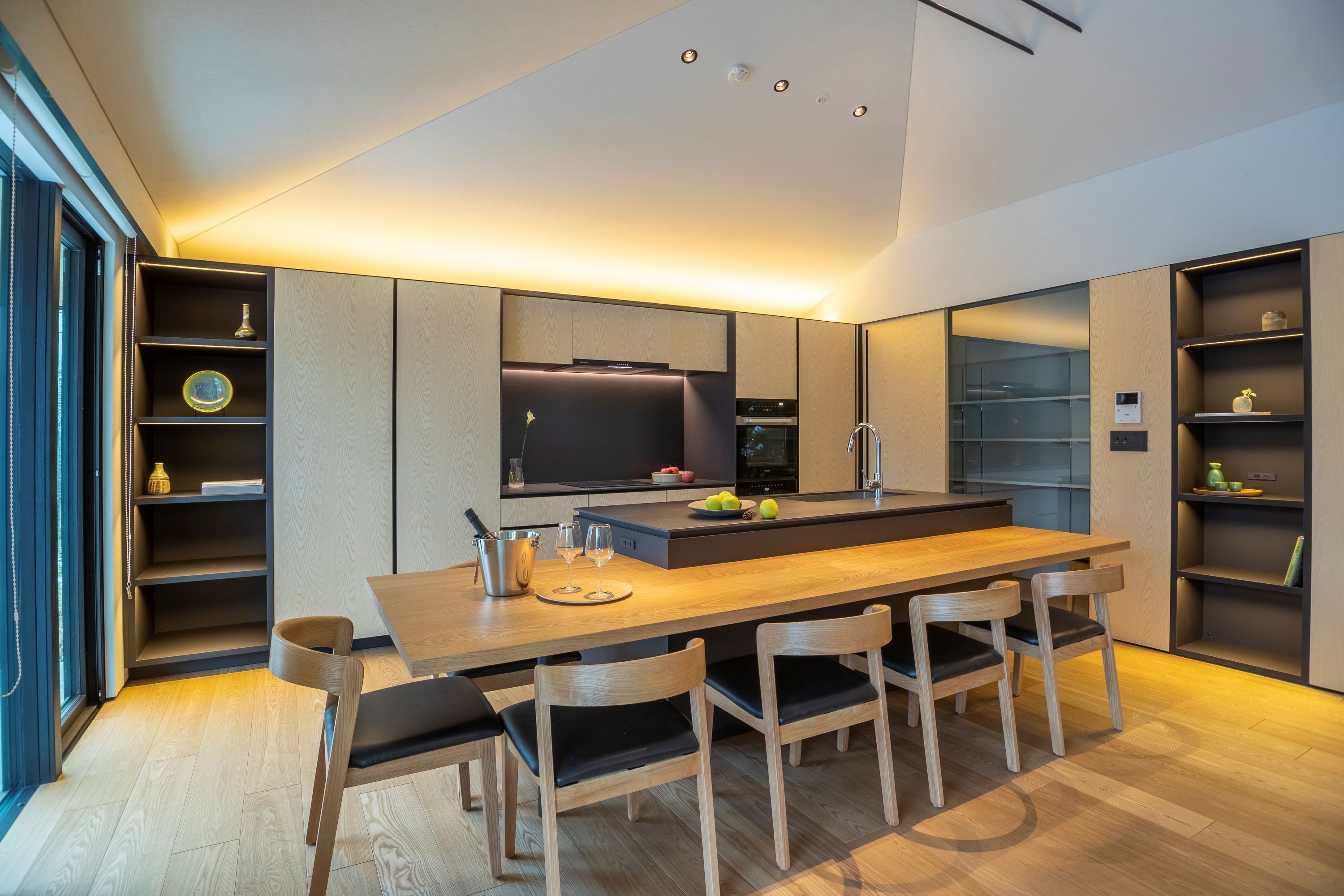 Una cocina moderna con una isla central, electrodomésticos integrados y un comedor con sillas de madera.