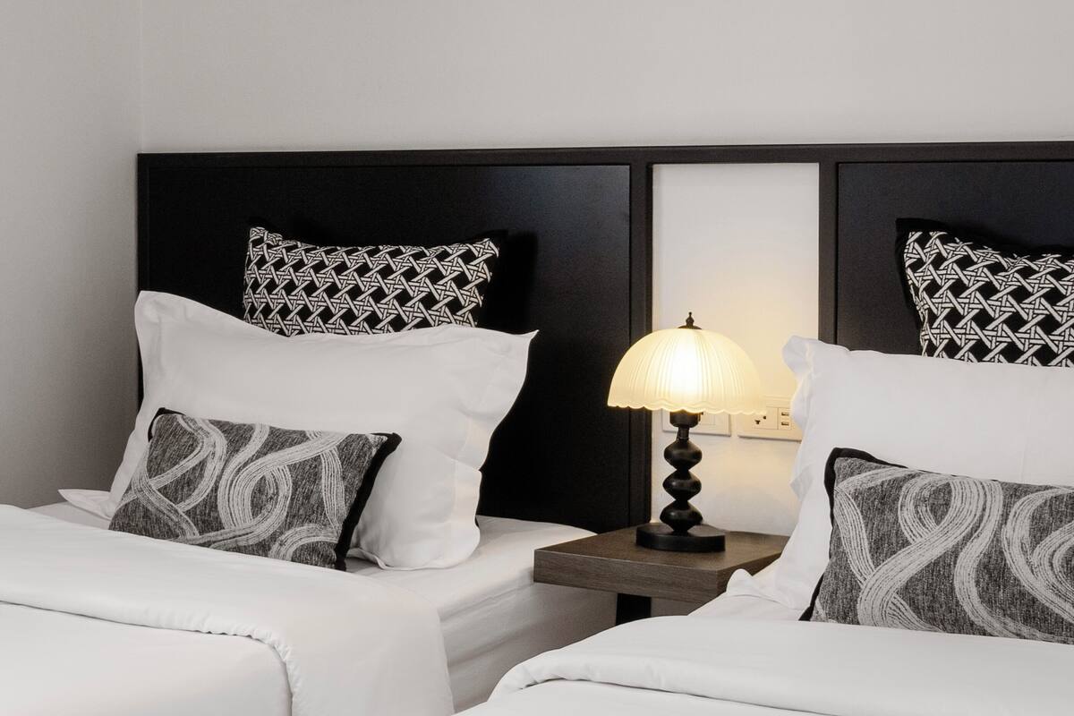 Quarto de hotel com duas camas, cabeceiras pretas, roupa de cama branca e uma obra de arte abstrata na parede.