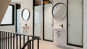 A modern bathroom with white brick walls, individual sinks with mirrors, and a glass door. - CASA BLANCA Dusit - Hostel (Bangkok)