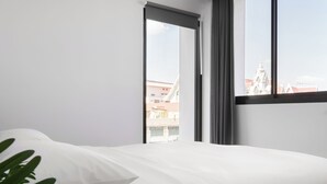 A bedroom with a bed, a window with a view of buildings, and a plant. - CASA BLANCA Dusit - Hostel (Bangkok)