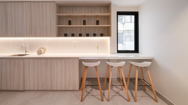 A modern kitchen with a central island, bar stools, and a window with a view. - CASA BLANCA Dusit - Hostel (Bangkok)