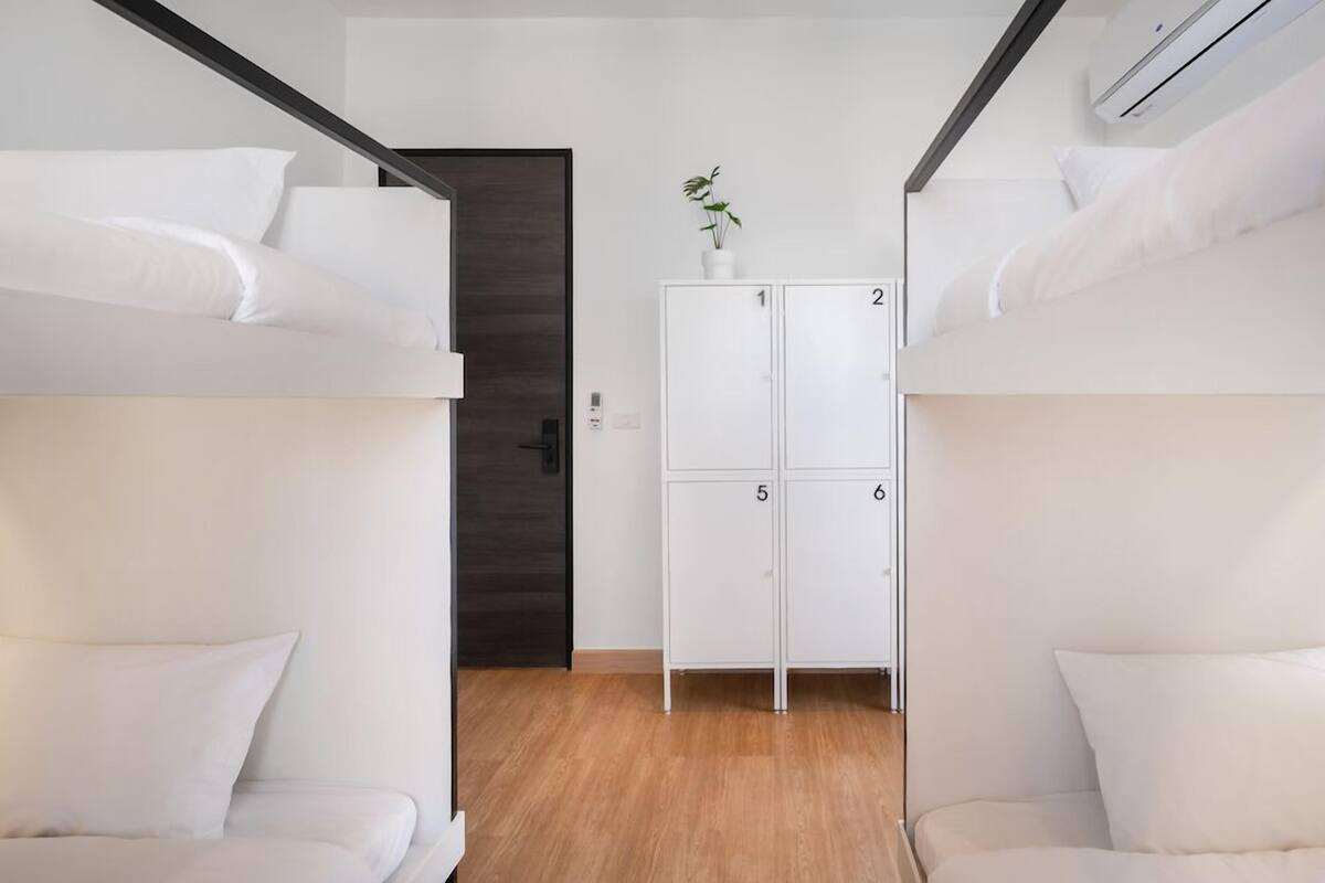 Quarto com beliches, piso de madeira, um armário branco com gavetas e uma porta.