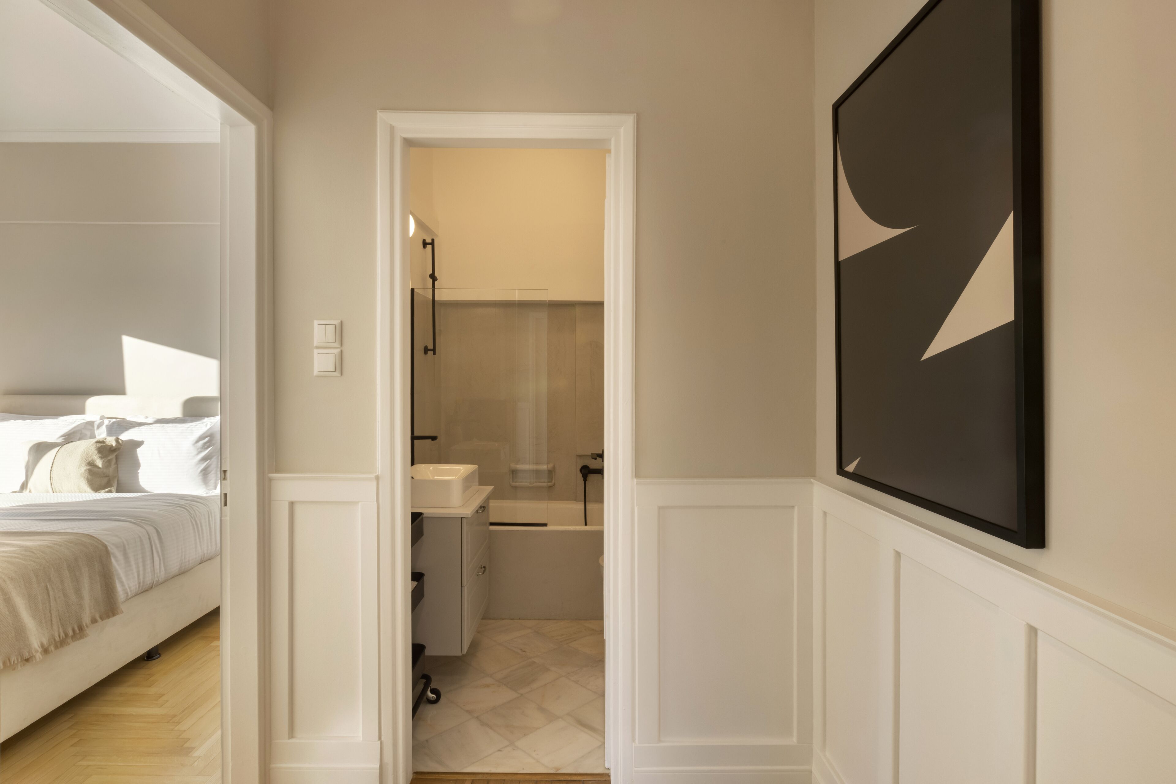 A hallway with a bed, a bathroom, and a framed artwork on the wall.