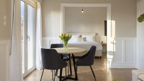 A modern hotel room with a large bed, a round table with chairs, and a vase of flowers. - Meliti Apartment in Plaka (Athens)