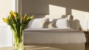 A bed with white linens and pillows, a bedside table with a lamp, and a vase with yellow flowers on a table. - Meliti Apartment in Plaka (Athens)