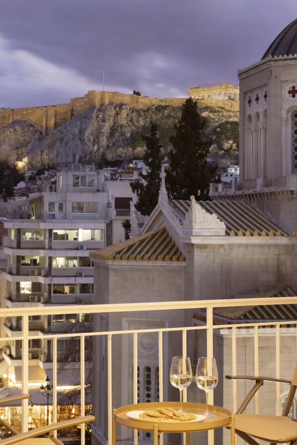 A balcony with a table set for two, overlooking a cityscape with historical architecture and a view of a hill. - Meliti Apartment in Plaka (Athens)