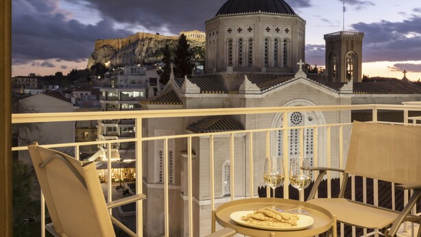 A balcony with a view of a historic building with a dome and a bell tower, a plate of food, and two wine glasses. - Meliti Apartment in Plaka (Athens)