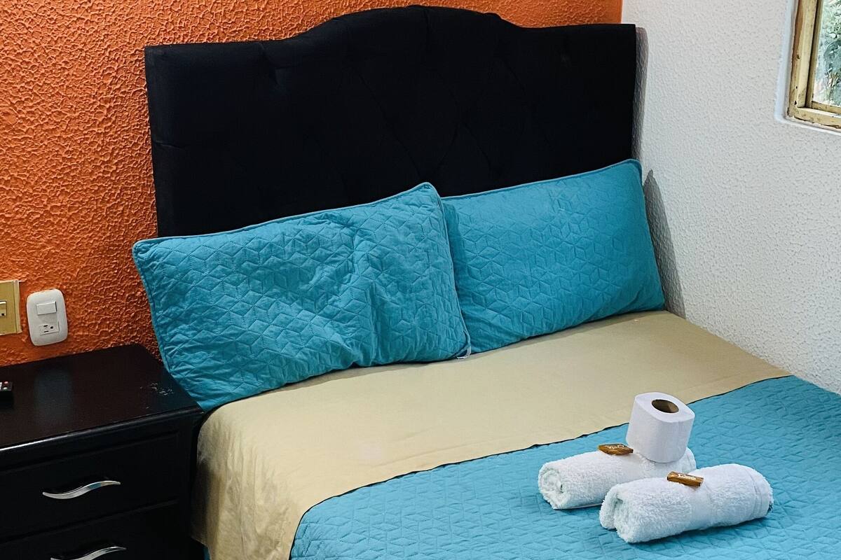 Une chambre à coucher comprenant un lit, une table de chevet et un mur avec un revêtement texturé de couleur orange.