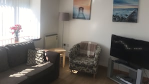 A living room with a sofa, a chair, a TV, and artwork on the wall. - Lovely 1-bed Cottage in Hopeman (Elgin)