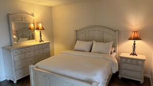 Une chambre à coucher avec un grand lit, deux tables de chevet avec des lampes, une commode et un miroir.