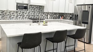 A modern kitchen with white cabinets, a large island with bar stools, stainless steel appliances, and pendant lighting. - Comfort by Southridge (Kennewick)