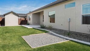 A modern single-story house with a well-maintained lawn and a gravel pathway leading to the entrance. - Comfort by Southridge (Kennewick)