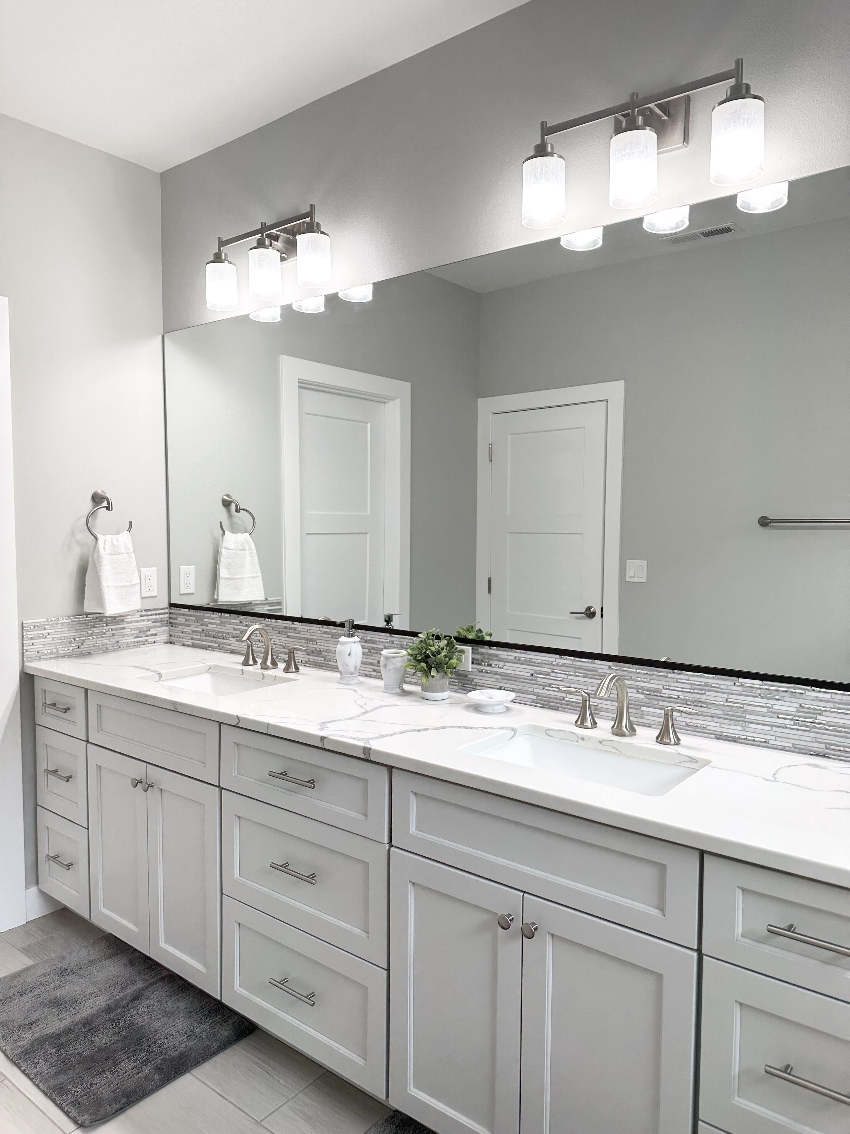 Une salle de bain moderne avec deux lavabos, un grand miroir et un luminaire placé au-dessus du miroir.