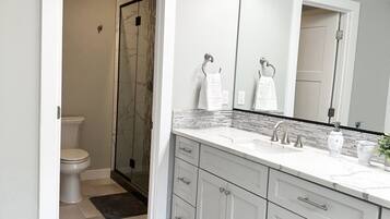 Un baño moderno con cabina de ducha, un espejo grande y tocador con lavamanos y toallero.