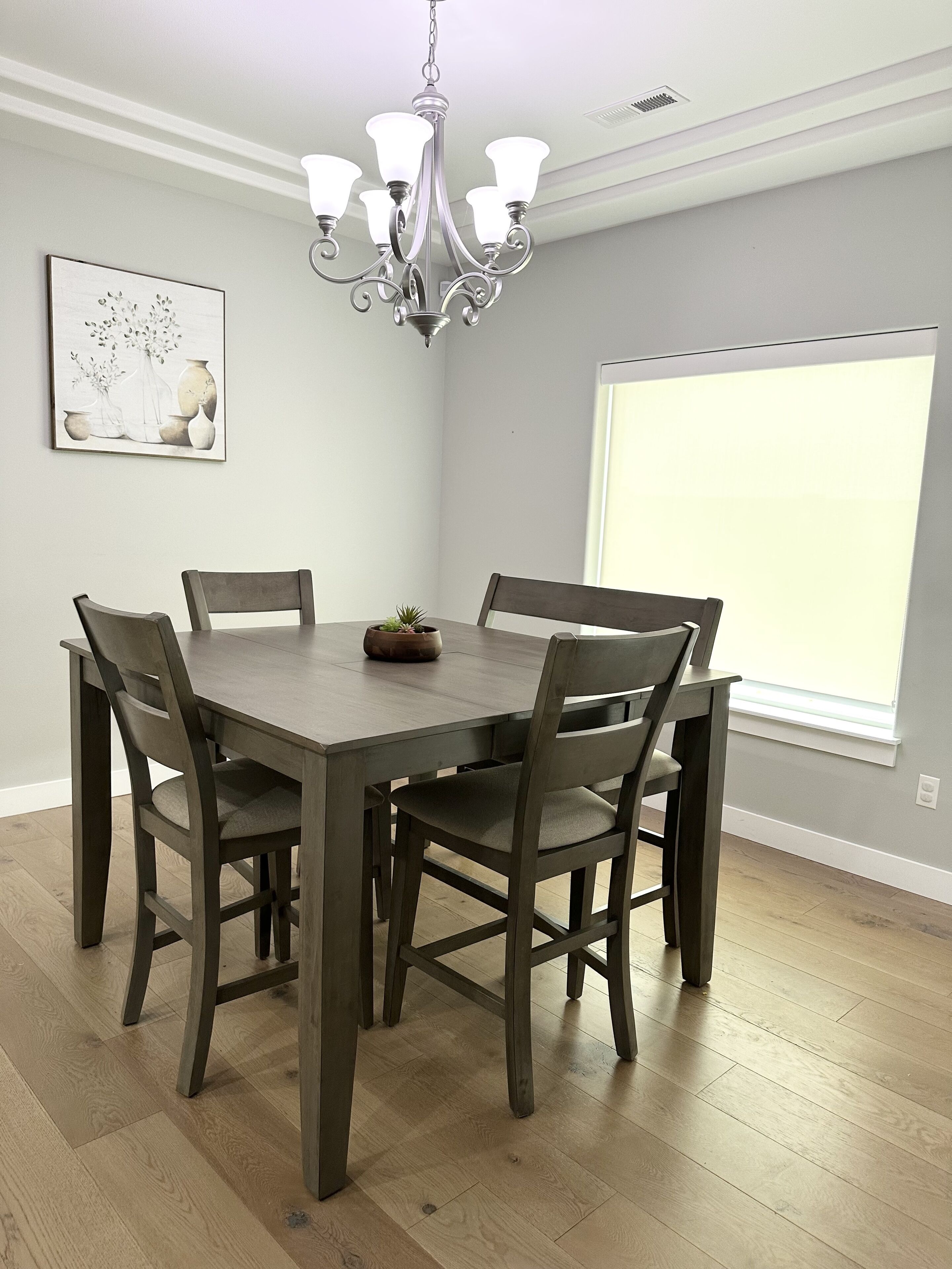 Un coin repas avec une table et des chaises en bois, un lustre, une fenêtre et une œuvre d’art accrochée au mur.