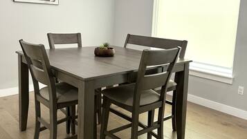 Un coin repas avec une table et des chaises en bois, un lustre, une fenêtre et une œuvre d’art accrochée au mur.