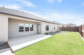 Een modern huis met één verdieping, een overdekt terras, een verzorgd gazon en een houten omheining.