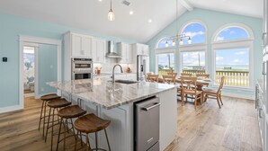 A spacious kitchen with a large island, white cabinetry, and a view to the outside. - Surfside - 2431 Bienville 4 Bedroom Home by RedAwning (Dauphin Island)