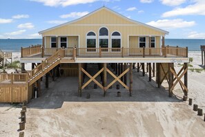 Uma casa de praia com varanda, deck de madeira e uma praia arenosa.