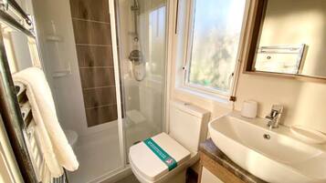 A bathroom with a glass-enclosed shower, a toilet with a green sign, a sink, and a window above the sink.