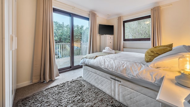 Ein Schlafzimmer mit Bett, Fernseher, Fenster und Balkon.