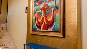 Un escalier menant à l’étage supérieur, une console bleue et un tableau coloré accroché au mur.