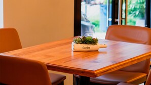 Une table en bois surmontée d’un jardinière portant l’inscription « Jardin », dans une pièce où se trouvent des chaises orange.