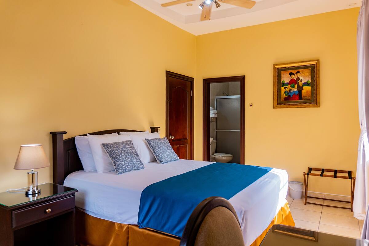 Una habitación de hotel con cama, mesita de noche y un cuadro en la pared.