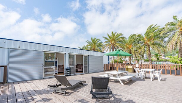 Une terrasse en bois avec des chaises longues, une table et un parasol vert.
