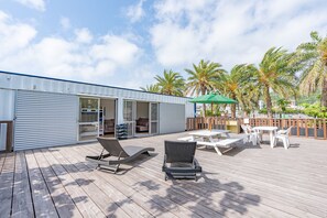 A wooden deck with lounge chairs, a table, and a green umbrella. - DUO Mermaid Stay (Nakagusuku)