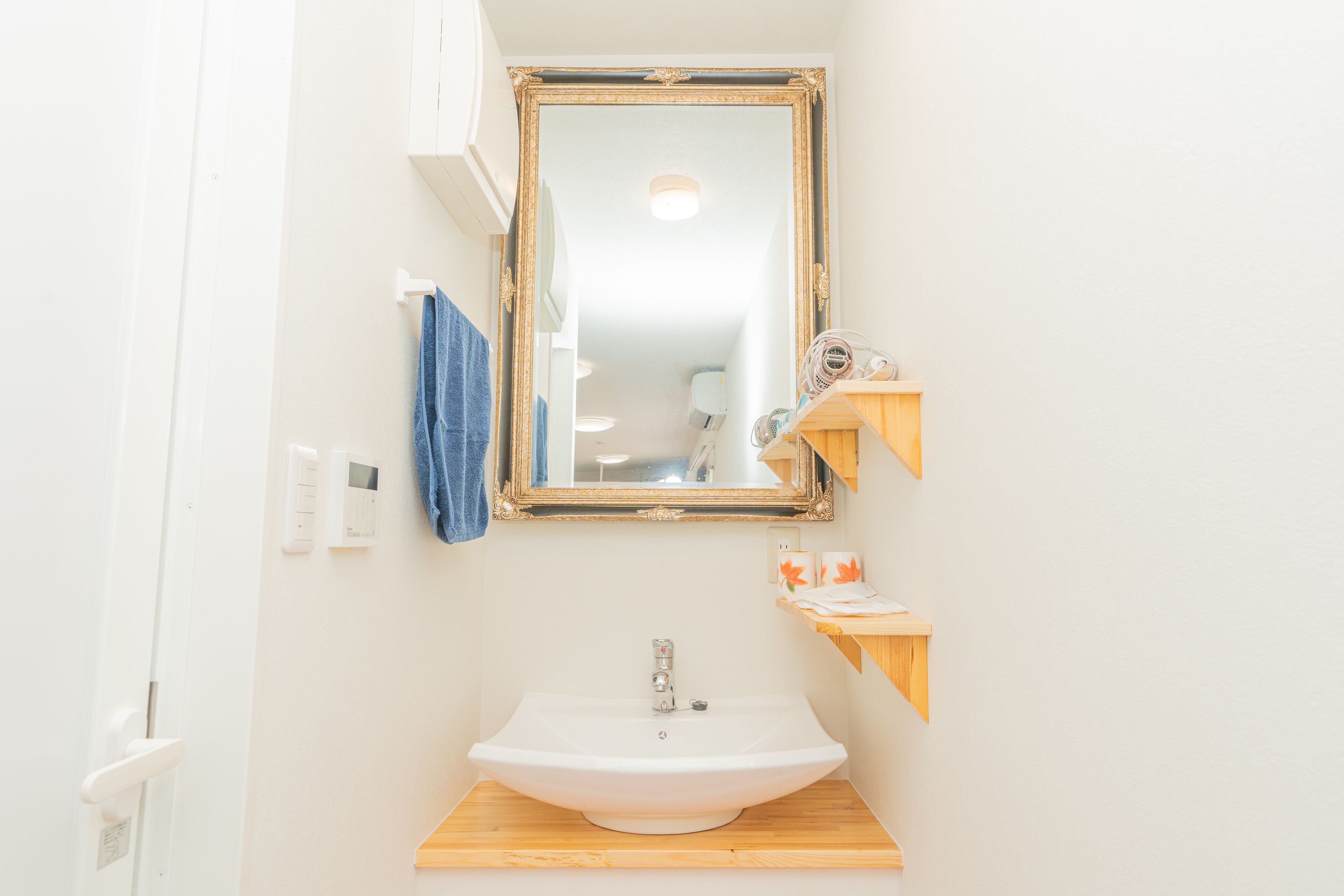 A bathroom with a white sink, a mirror with a gold frame, and wooden shelves.