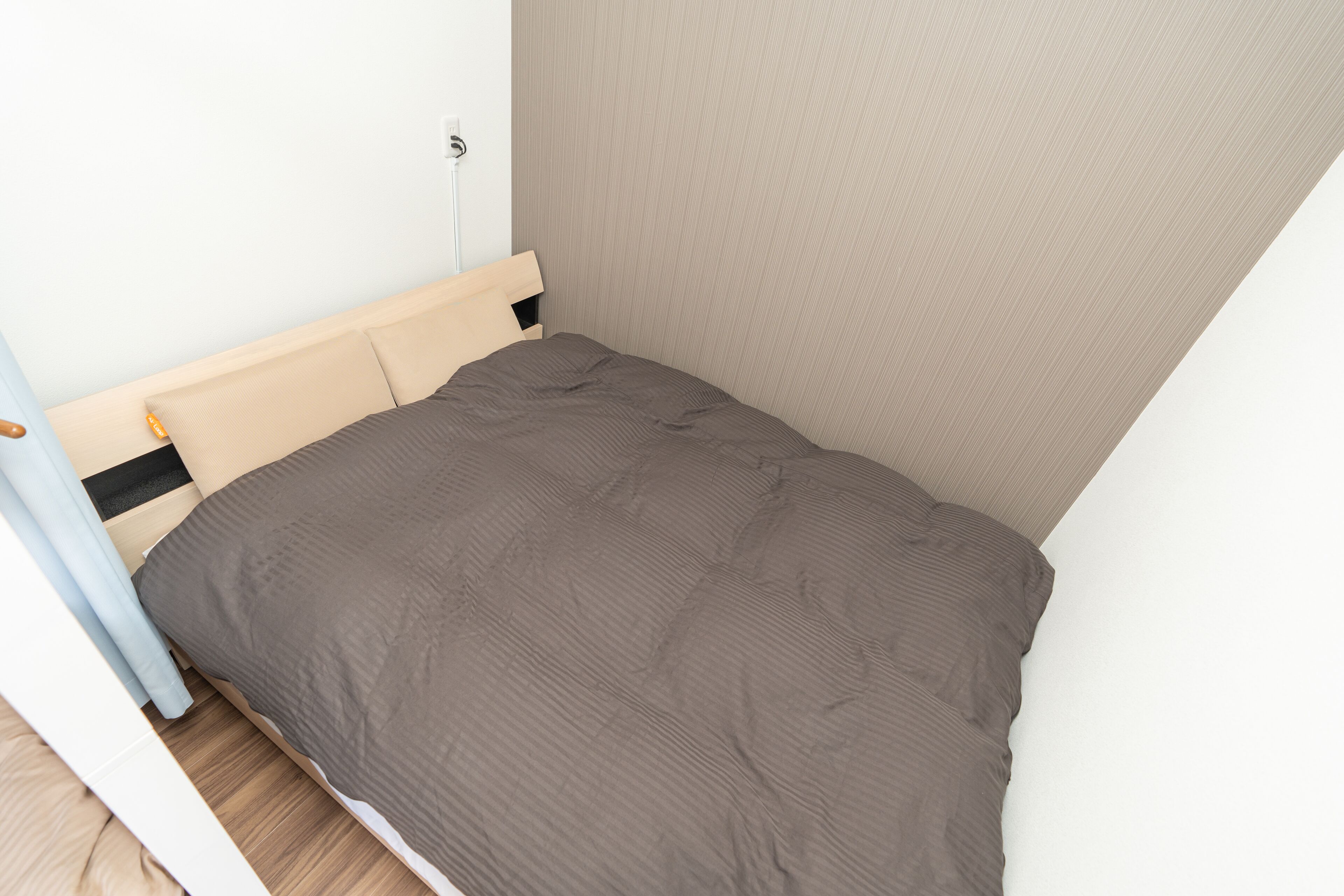 Una habitación pequeña con cama individual, cabecera de madera, pared color beige y suelo de tono claro.