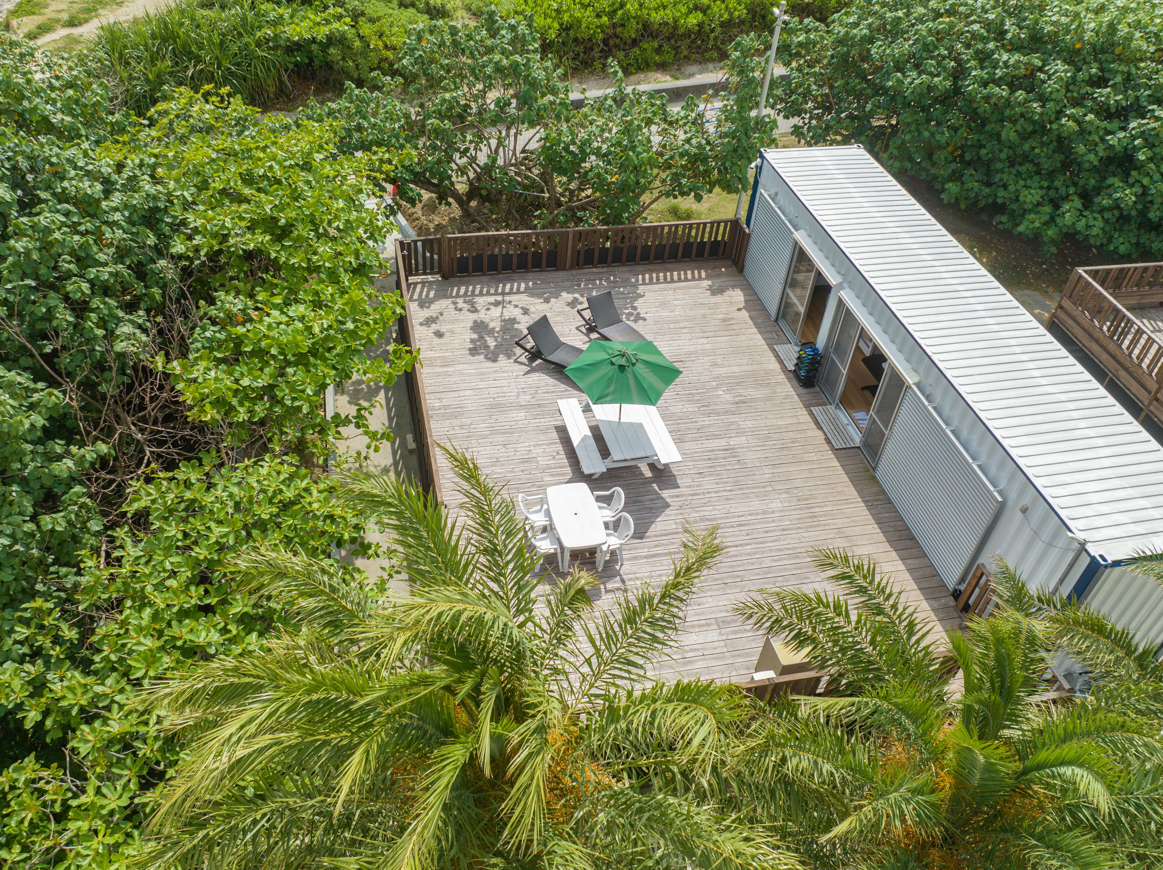 Vista aérea de una propiedad con un patio que tiene una mesa y sillas, una sombrilla verde y un edificio con techo metálico.
