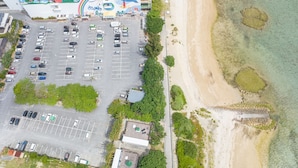 Vue aérienne d’un parking situé à côté d’une plage, avec une eau claire et quelques zones de végétation.