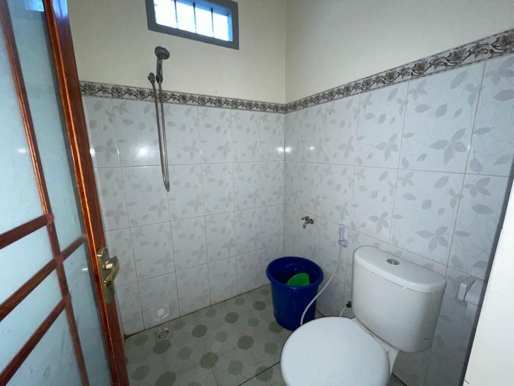 A small bathroom with a toilet, a shower, and a blue bucket.