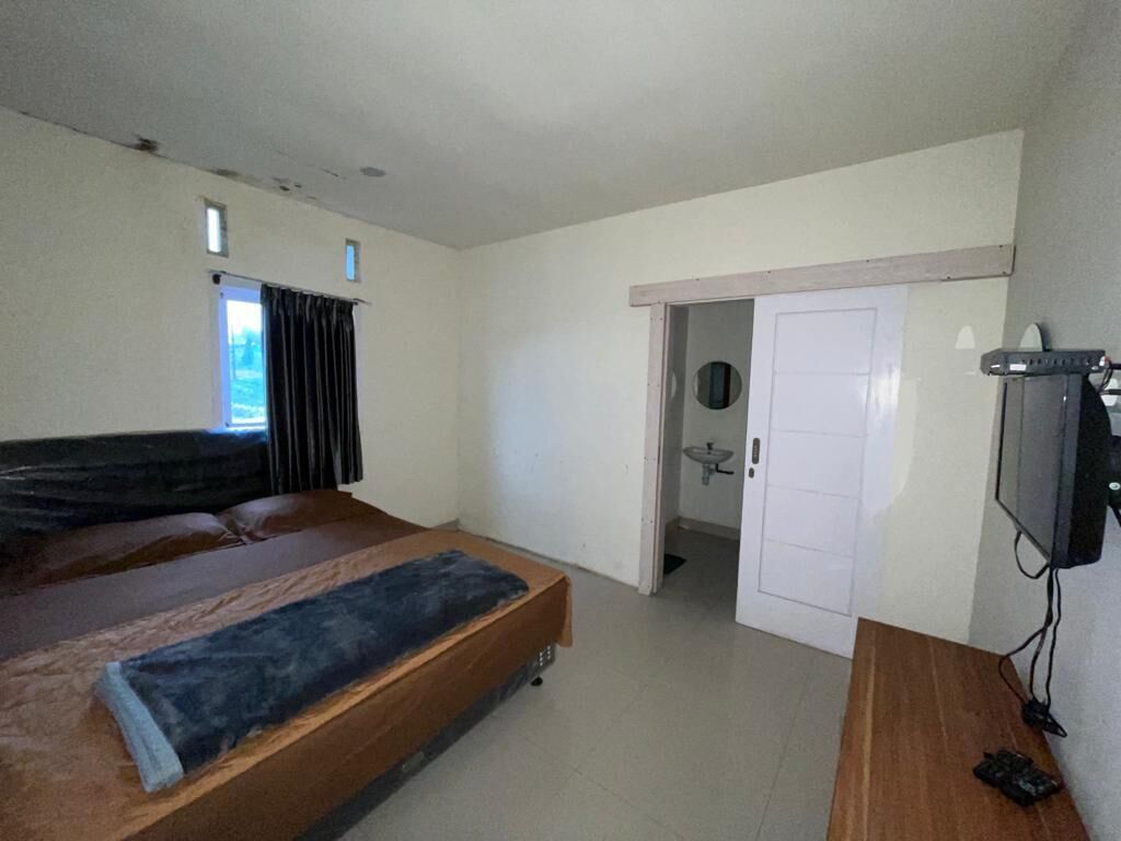 A bedroom with a bed, a desk, a television, and a door leading to another room.