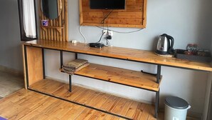 Una habitación con escritorio de madera, televisor montado, tetera y cubo de basura.