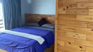 Un dormitorio con cabecera de madera, cama con ropa de cama azul y una ventana con cortinas.