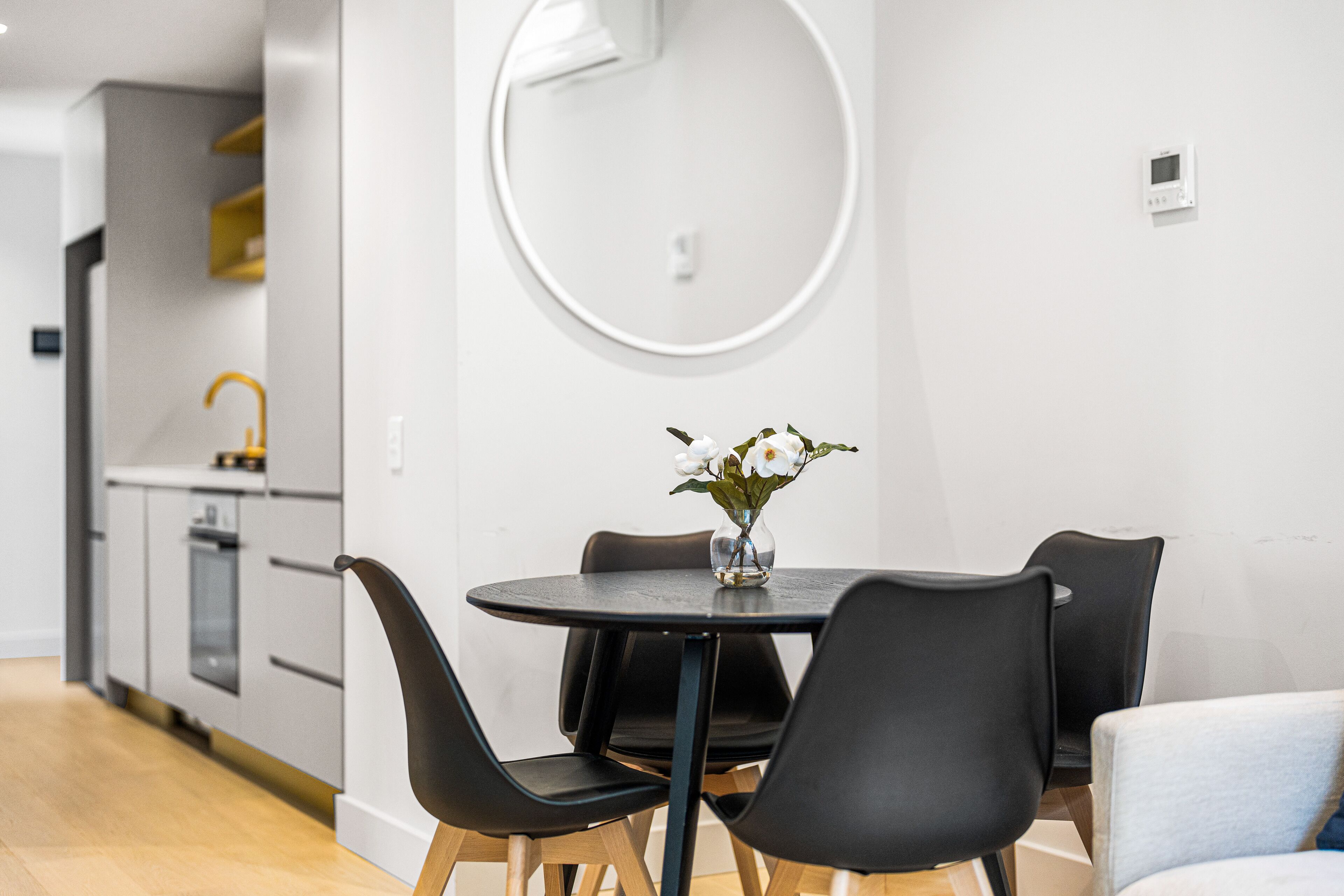 A modern kitchen with a round mirror, a dining table with chairs, and a vase with flowers.