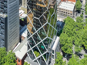 A high-rise building with a distinctive geometric glass facade, surrounded by urban streets and greenery. - Paragon Apartments by CLLIX (Melbourne)