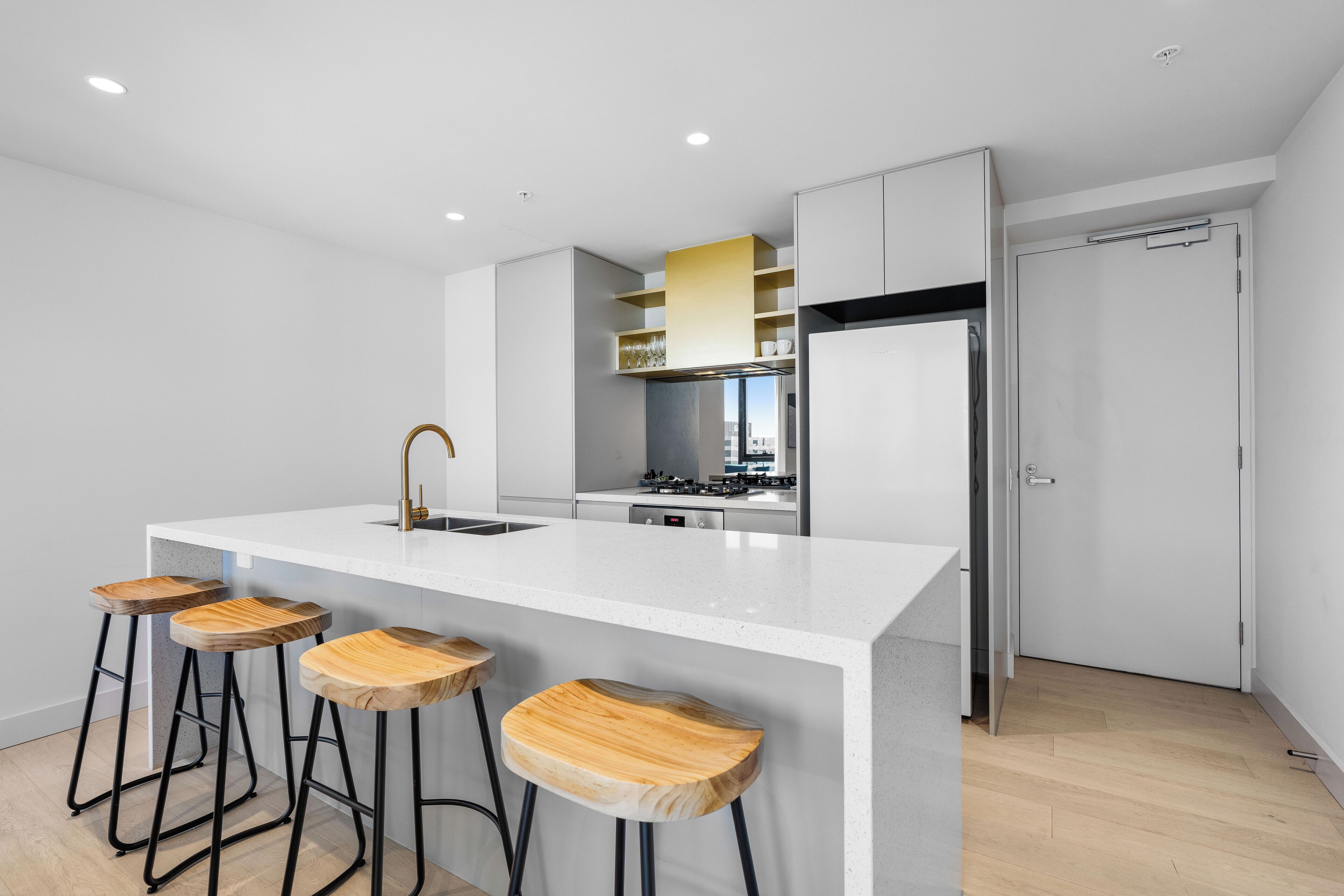 Une cuisine moderne avec un îlot central blanc, des tabourets en bois et des appareils électroménagers en acier inoxydable.