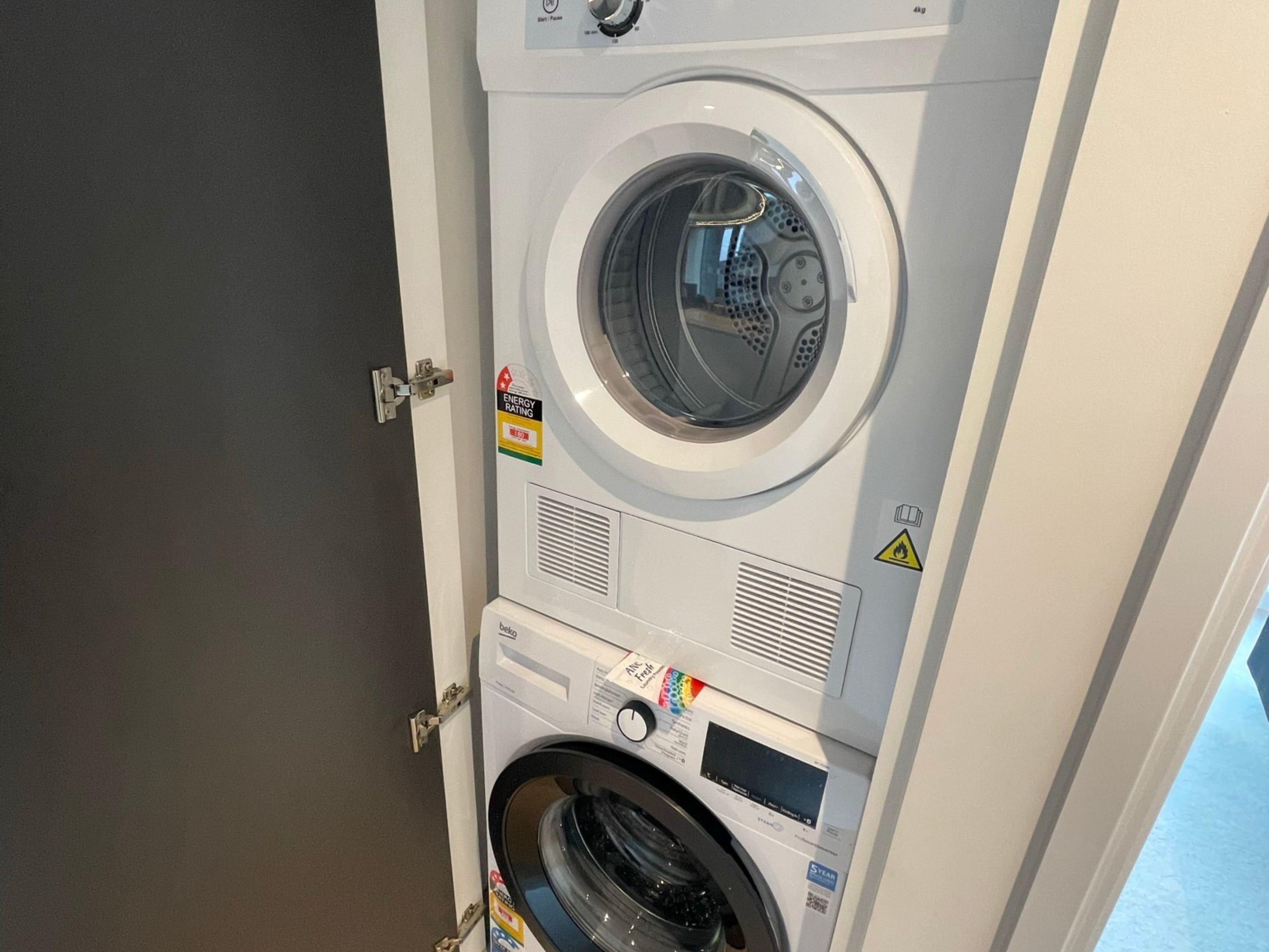 A front view of a stacked washer and dryer unit with a door partially open.