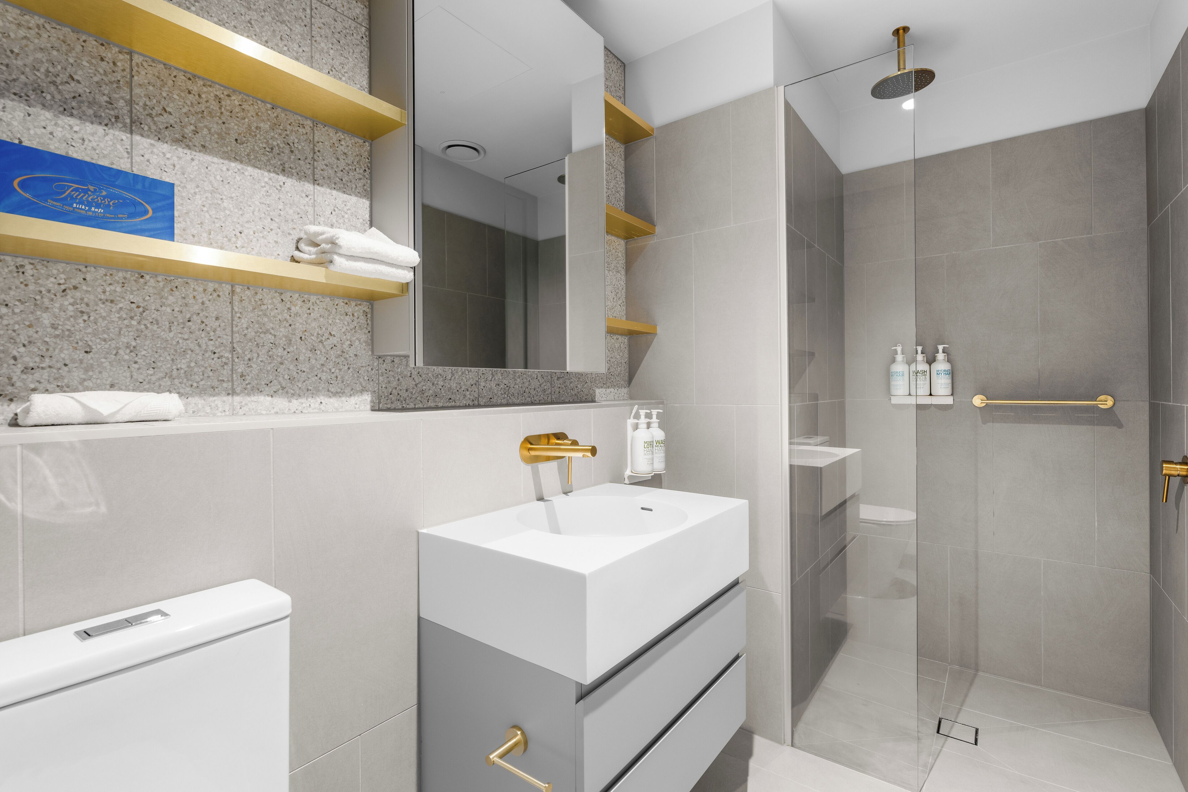 A modern bathroom with a white sink, gold fixtures, and a glass-enclosed shower.