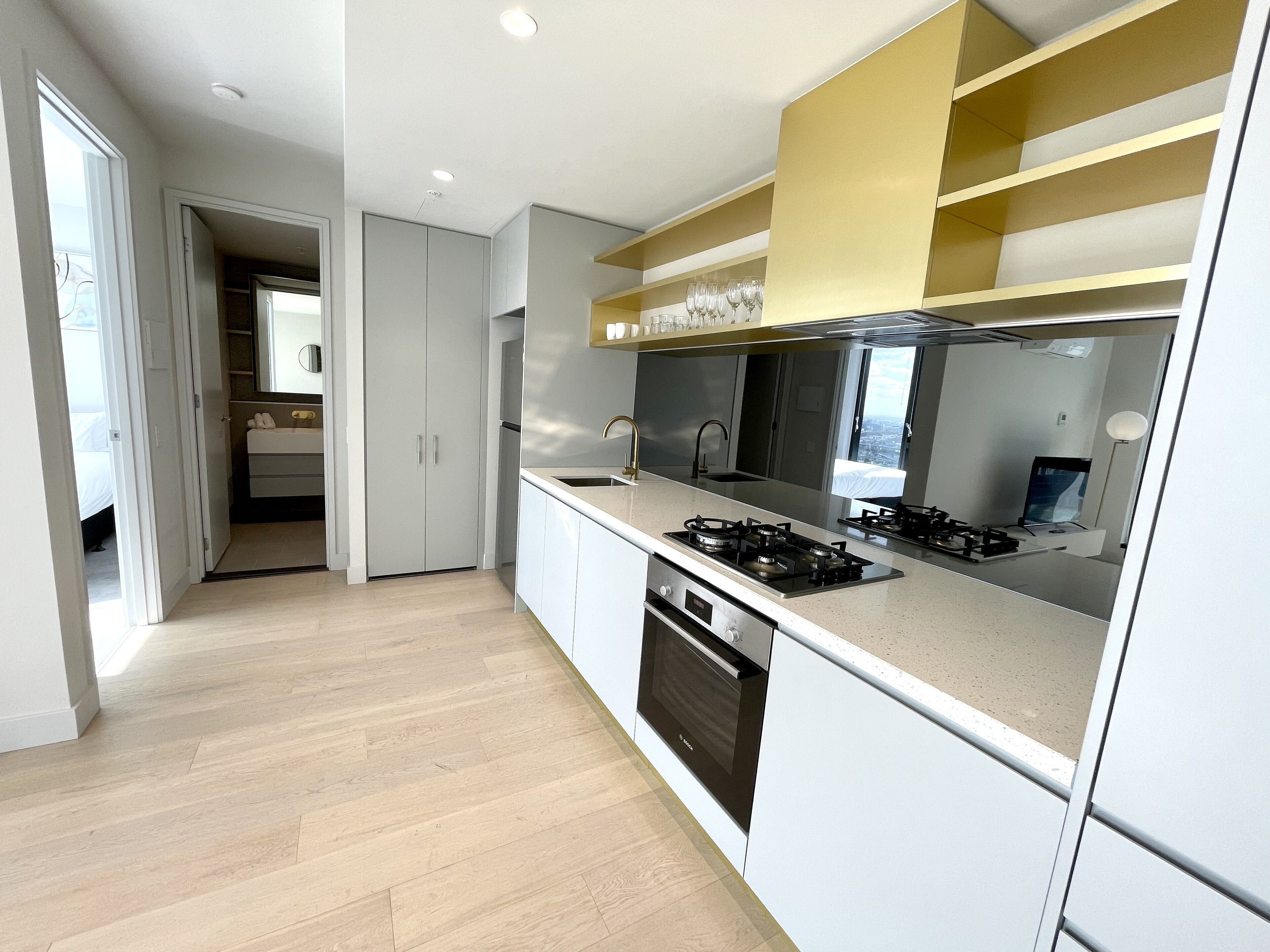 A modern kitchen with a gas stove, oven, and a built-in sink. There is a small window above the sink and a door leading to a bathroom.