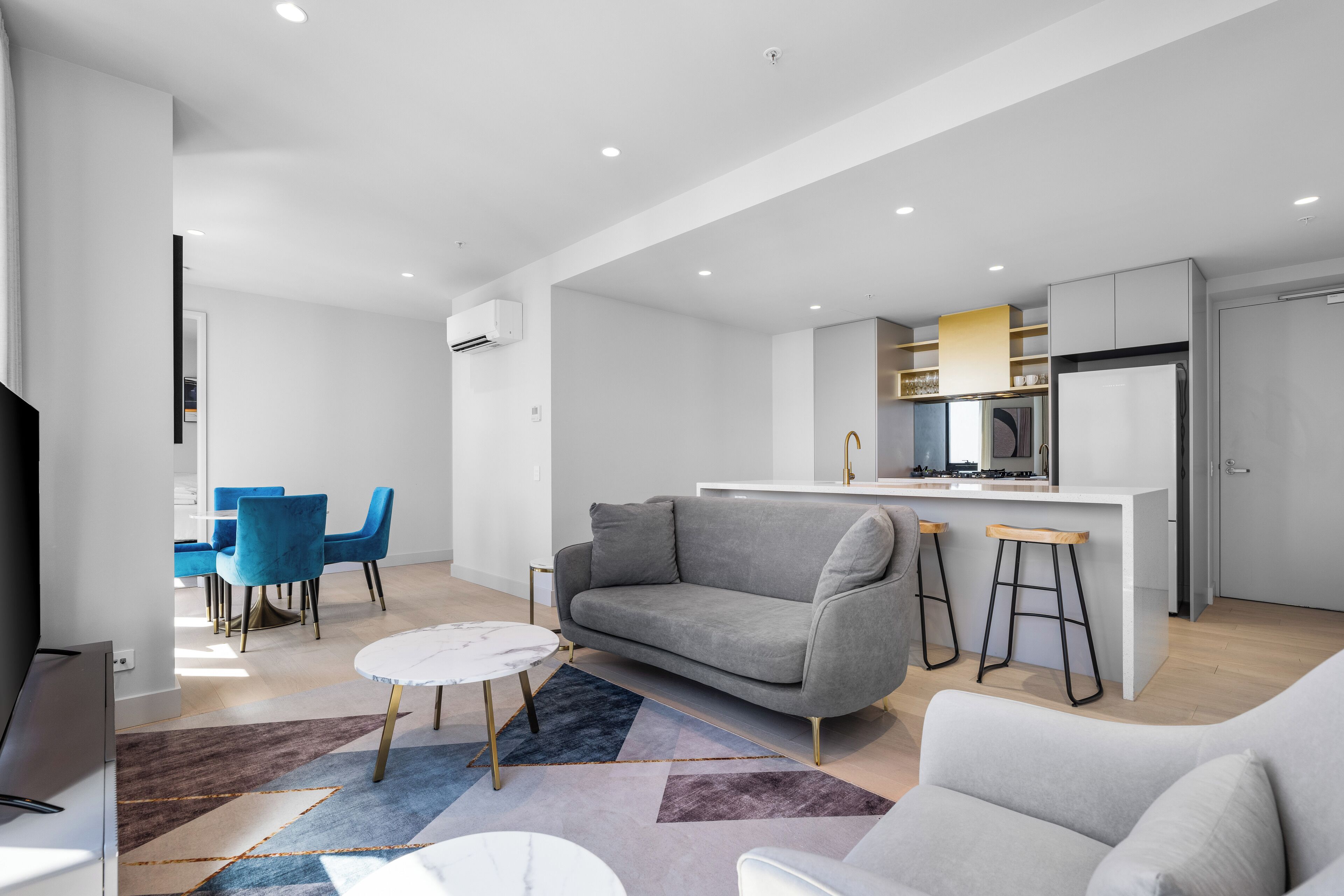 A modern living room with a grey sofa, a coffee table, and a dining area with blue chairs.