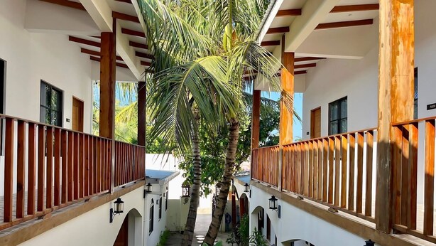 A covered walkway with wooden railings, palm trees, and arched doorways. - Ahiva Village (Fulhadhoo)
