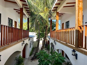 A covered walkway with wooden railings, palm trees, and arched doorways. - Ahiva Village (Fulhadhoo)