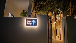 A sign for 'Aloha Village' with a neon logo, a gated entrance, and a pathway leading to a building with a wooden staircase. - Ahiva Village (Fulhadhoo)