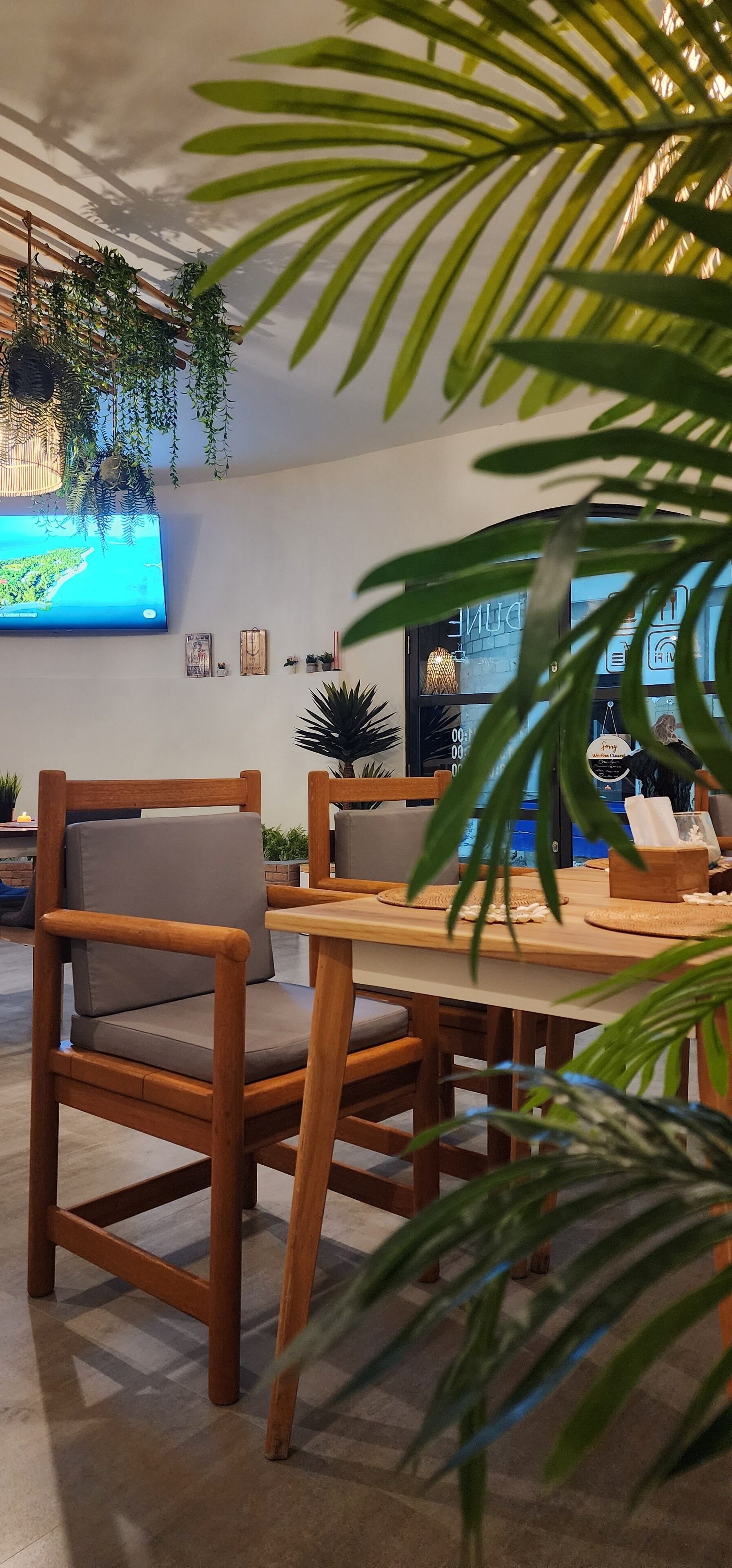 Ein modernes Interieur mit einem Holzes Esstisch und Stühlen, einem an der Wand befestigten Flachbildfernseher und verschiedenen Zimmerpflanzen.